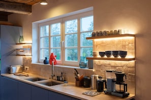 Une cuisine avec une fenêtre, un évier, une machine à café et divers ustensiles de cuisine.
