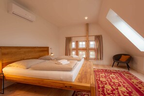 A bedroom with a wooden bed, a red patterned rug, a chair, and a window with curtains. - NEW: HackmannsHof. Half-timbered courtyard in the countryside. (Ankum)