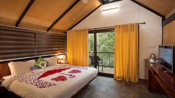 Een slaapkamer met een groot bed, een televisie, een houten plafond en een balkon met gordijnen.