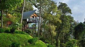 A two-story wooden cabin with a balcony, surrounded by lush greenery and trees. - Bamboo Dale Resort (Udumbanchola)