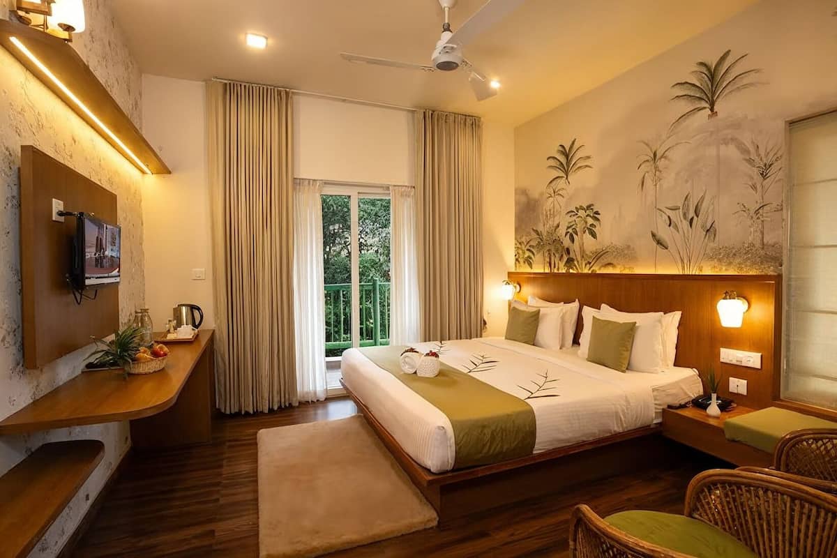 Habitación de hotel con cama, televisor, escritorio con computadora, silla y ventana con cortinas.