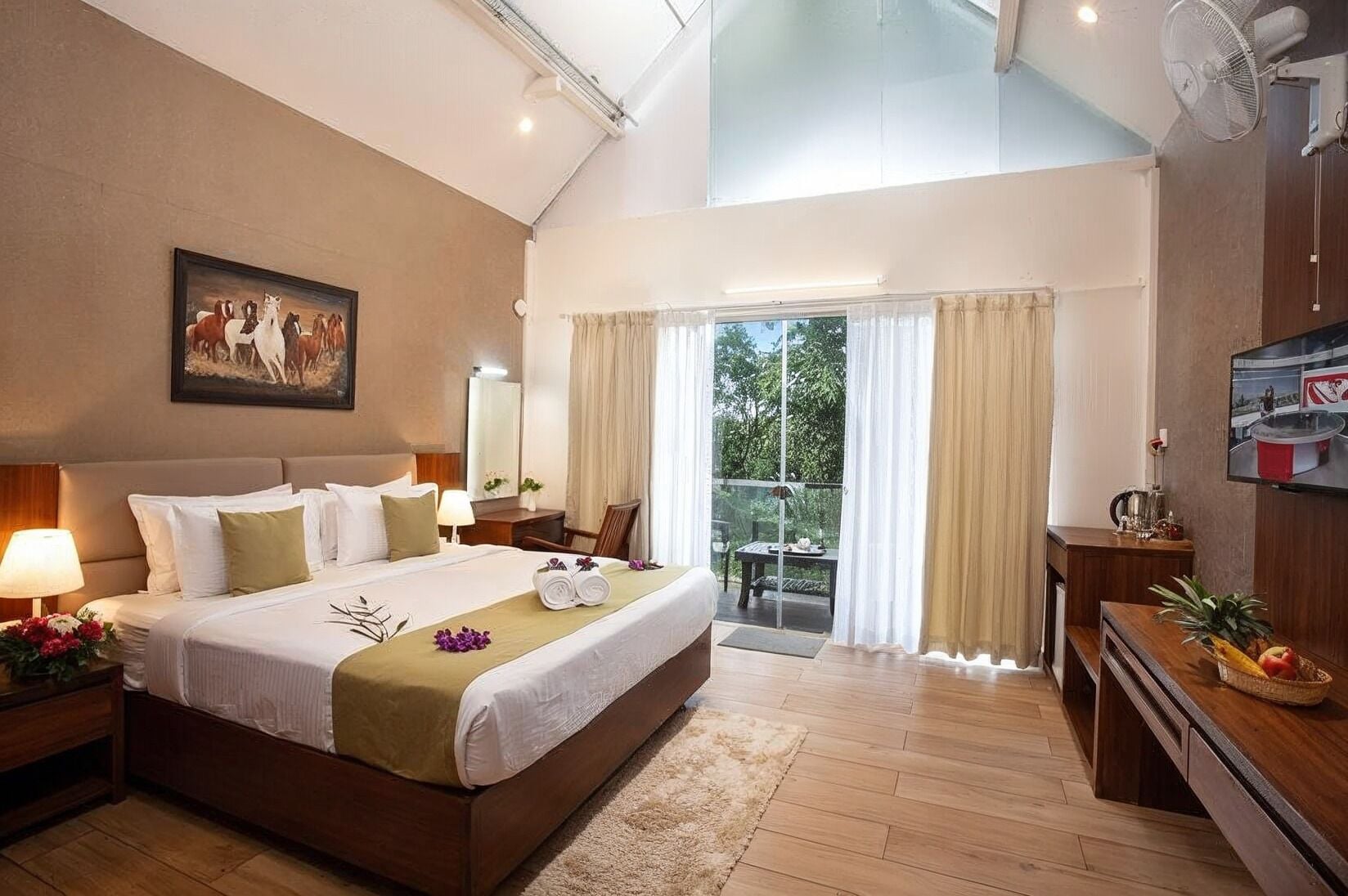 A spacious bedroom with a large bed, a sitting area with a TV, and a balcony with curtains.