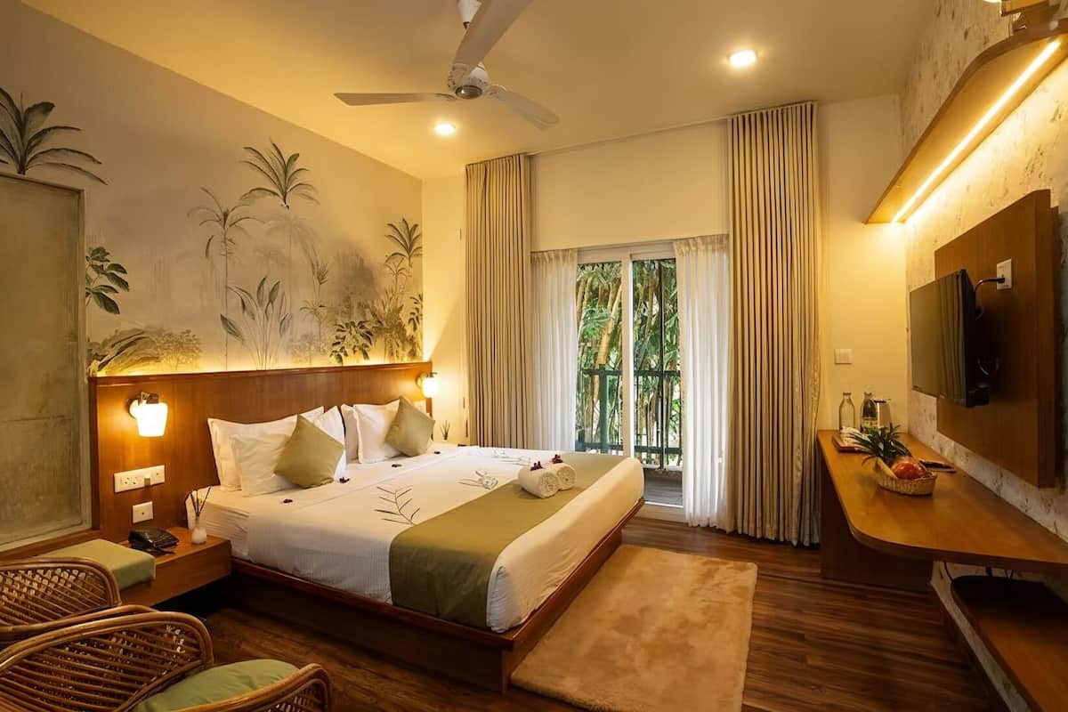 Habitación de hotel con cama, escritorio, silla, ventilador de techo y vistas a zonas verdes por la ventana.