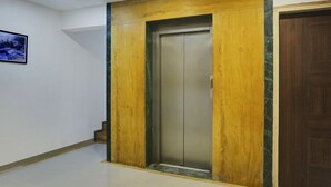 An elevator in a hallway with a wooden panel design and a marble accent. - Hotel Orchard Park (Pune)
