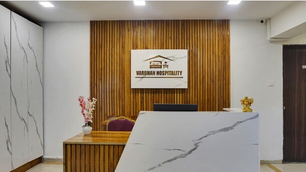 A reception area with a marble reception desk, a wooden panel wall, and a sign for Vardhan Hospitality. - Hotel Orchard Park (Pune)