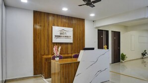 A reception area with a wooden panel wall, a reception desk, and a logo for Vardhan Hospitality. - Hotel Orchard Park (Pune)