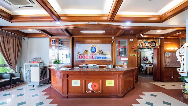 Zona de recepción de un hotel con un mostrador de madera, un cartel que indica Hotel Cowboy y un mostrador con varios artículos.