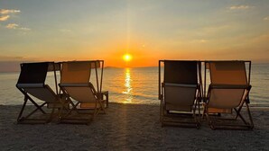 Een strand met vier ligbedden gericht op de zee tijdens zonsondergang.