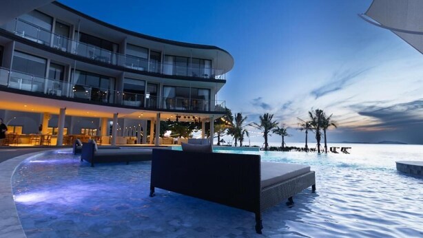 Een modern hotel met een zwembad, terras en uitzicht op de oceaan in de schemering.