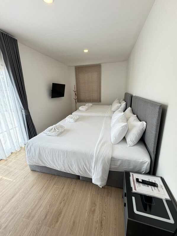 A hotel room with a large bed, a flat-screen TV, a bedside table with a remote control, and a window with blinds. - Atlantis Manor (Chonburi)