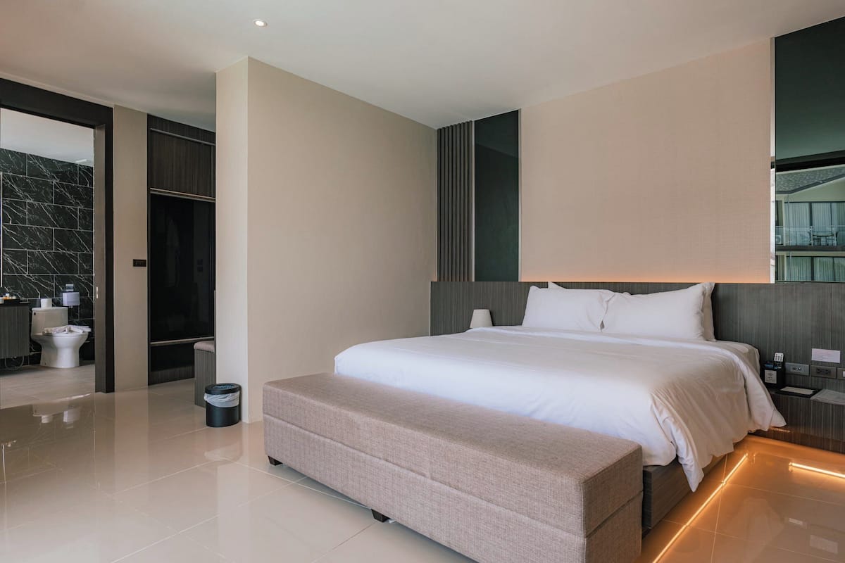 Une chambre d’hôtel moderne avec un grand lit, une table de chevet, une commode, un miroir et une vue sur la ville.