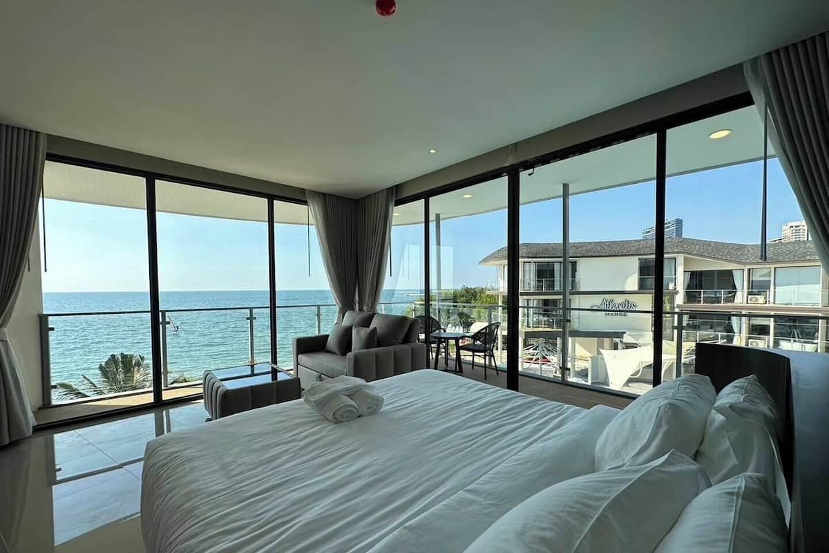 Une chambre d’hôtel moderne dotée d’un grand lit, d’un coin salon avec une table et d’un balcon offrant une vue sur la mer et un bâtiment.