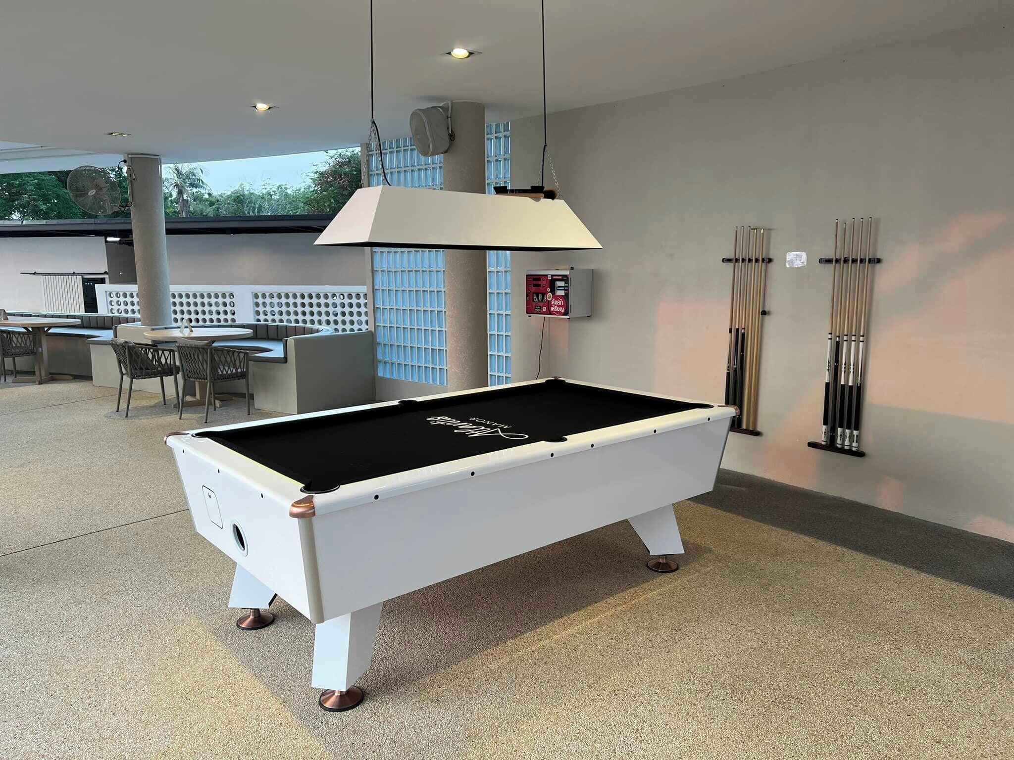 A pool table in a well-lit indoor space with a ceiling fan, a seating area with a table and chairs, and a wall-mounted cue rack.