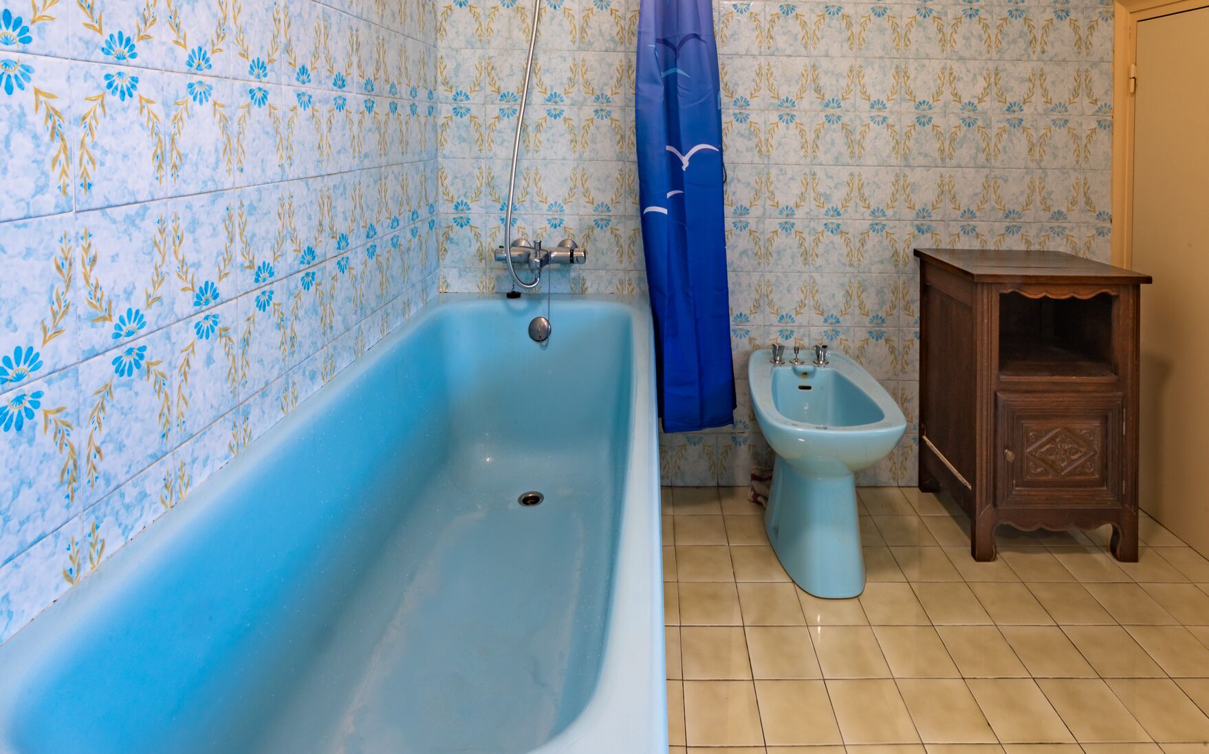 A bathroom with a bathtub, a bidet, and a wooden cabinet.