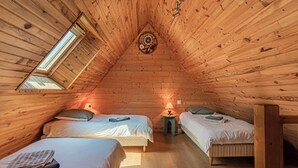 Un dormitorio acogedor en el ático con dos camas, paredes de madera, un tragaluz y un medallón decorativo en el techo.