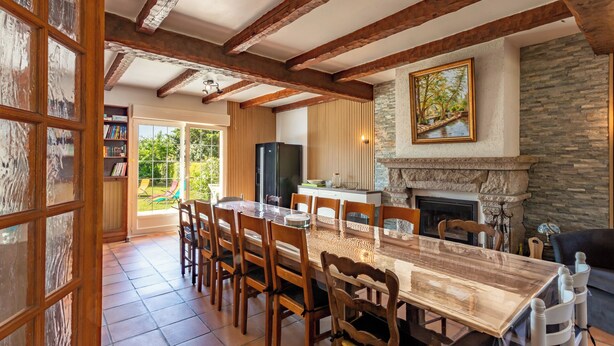 Un comedor con mesa y sillas de madera, chimenea de piedra y vista al exterior.