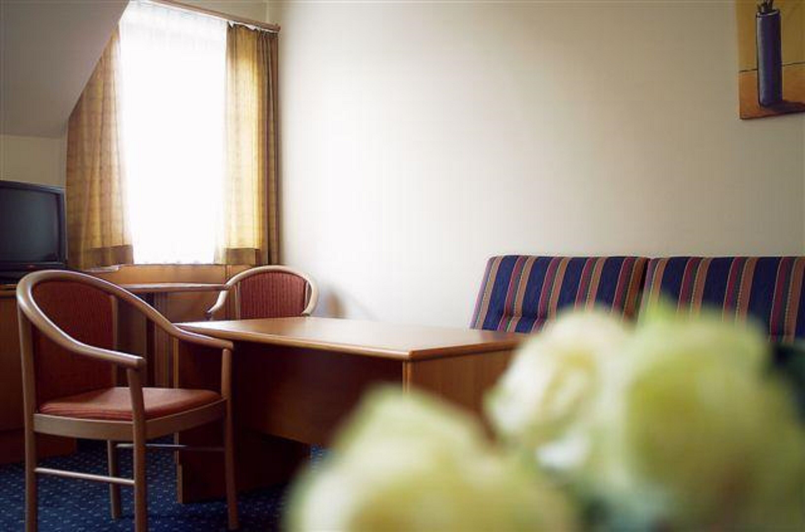 Una habitación de hotel con cama, escritorio, dos sillas, televisor y ventana con cortinas.