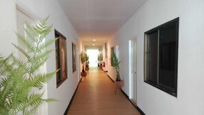 Un pasillo largo y estrecho con suelo de madera, paredes blancas y ventanas con marcos negros.