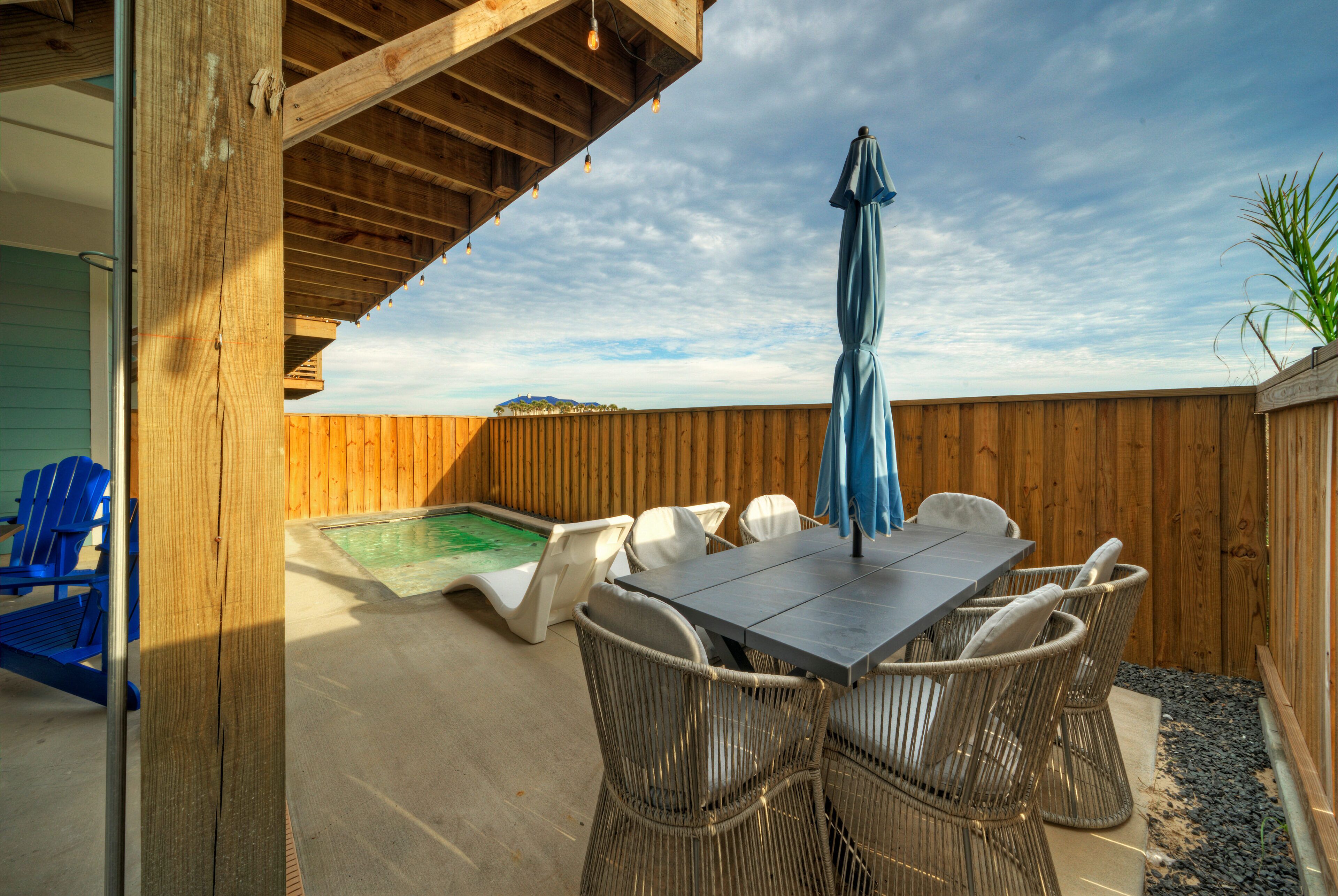 A wooden deck with a pool table, wicker chairs, and a blue umbrella.