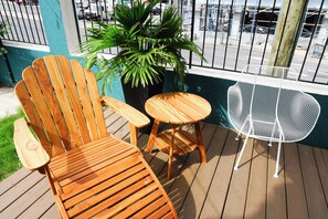 Eine Holzterrasse mit einem Holzstuhl, einem kleinen runden Tisch und einem weißen Metallstuhl.