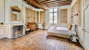 A room with a wooden floor, a bed, a dresser, a mirror, and a fireplace. - Live the Chateau Dream in the Loire Countryside (Bazouges-sur-le-Loir)