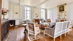 A spacious room with a fireplace, multiple seating options including a sofa and chairs, a large mirror, and a decorative vase with flowers. - Live the Chateau Dream in the Loire Countryside (Bazouges-sur-le-Loir)