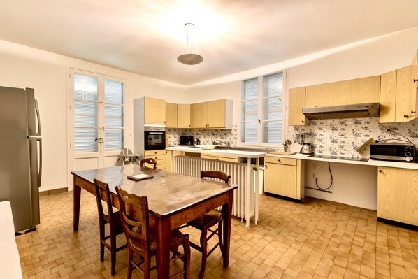 A kitchen with wooden cabinets, a built-in oven, a refrigerator, and a dining table with chairs. - Live the Chateau Dream in the Loire Countryside (Bazouges-sur-le-Loir)