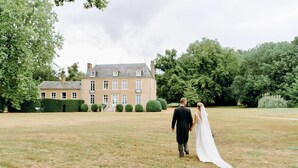 A couple walking on a grassy lawn in front of a large, historic building with multiple windows and a well-maintained garden. - Live the Chateau Dream in the Loire Countryside (Bazouges-sur-le-Loir)