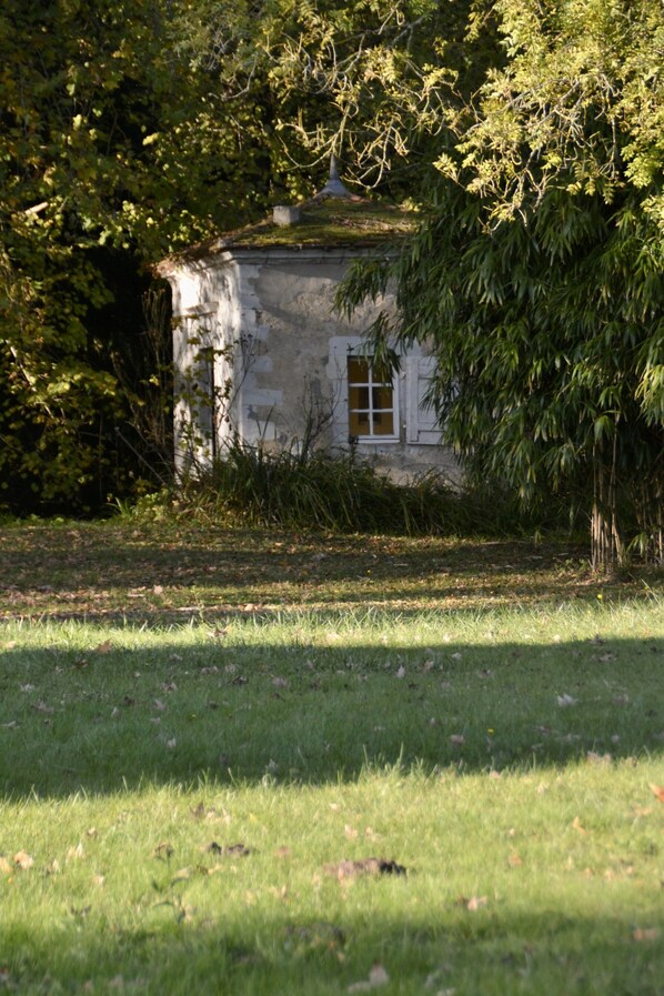 A rustic, single-story building with a small window, surrounded by lush greenery and trees. - Live the Chateau Dream in the Loire Countryside (Bazouges-sur-le-Loir)
