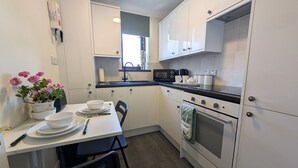 A compact kitchen with white cabinets, a microwave, a stove, and a dining table with chairs. - 19 Seaview Bay-Isle of Wight (Seaview)