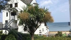 A white building with a staircase and balconies, a palm tree in front, and a view of the sea. - 19 Seaview Bay-Isle of Wight (Seaview)