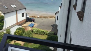 A view from a balcony overlooking a beach with a parked car and a building with a white facade.