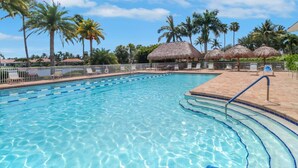 A clear swimming pool with lane dividers, surrounded by lounge chairs and palm trees.