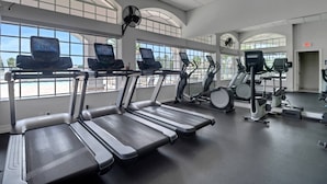 A gym with treadmills, elliptical machines, and exercise bikes, large windows, and a ceiling fan.