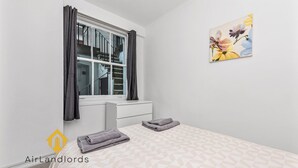 A bedroom with a bed, a window with curtains, a painting on the wall, and a logo. - Exclusive 4 bedroom apartment in Russell Square (Greater London)