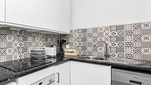 A modern kitchen with white cabinets, a black countertop, and patterned backsplash tiles. - Exclusive 4 bedroom apartment in Russell Square (Greater London)