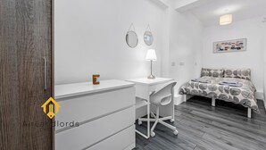 A modern bedroom with a wooden wardrobe, a desk with a lamp, a bed with a patterned bedspread, and a wall-mounted mirror. - Exclusive 4 bedroom apartment in Russell Square (Greater London)