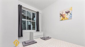 Een slaapkamer met een bed, een raam met gordijnen, een schilderij aan de muur en een logo.