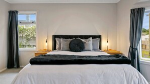 Ein Schlafzimmer mit einem großen Bett, zwei Nachttischen, einer Kopfteil und einem Fenster mit Vorhängen.
