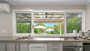 Eine moderne Küche mit großem Fenster, integriertem Geschirrspüler, Backofen und Blick auf Grünflächen.