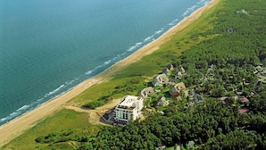 An aerial view of a coastal property with a beach, green landscape, and a large white building with multiple stories. - Kustenwaldvilla in Dierhagen (Ostseebad Dierhagen)