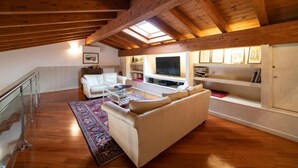 A spacious loft with a high ceiling, wooden beams, a large window, a white sofa, a TV, and a bookshelf. - ROMANTIC LAKE VIEW HOUSE (Sulzano)