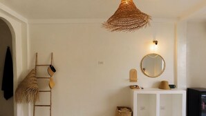 A minimalist room with a woven light fixture, a ladder, a woven basket, a round mirror, and a white console table. - The Hidden Home (Patong)