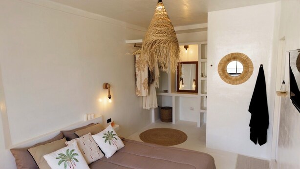 A bedroom with a bed, a hanging light fixture, a mirror, and a towel rack. - The Hidden Home (Patong)