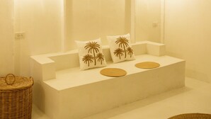A minimalist bathroom with a large mirror, two palm tree pillows, and a woven basket. - The Hidden Home (Patong)