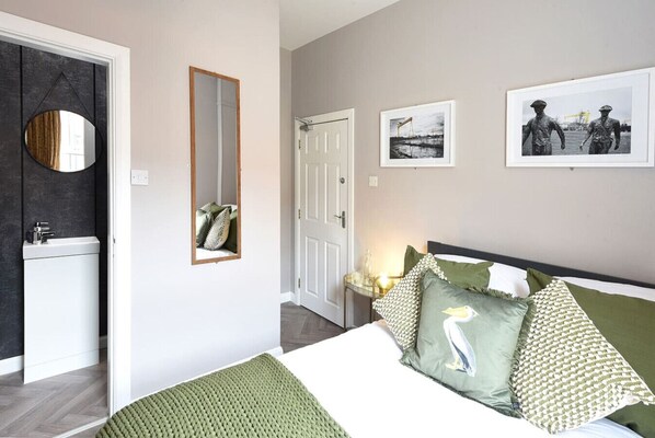 Un dormitorio con cama, almohadas, un espejo, una puerta y obras de arte en la pared.