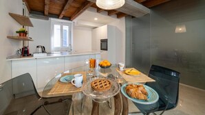 A modern kitchen with white cabinets, a wooden ceiling, and a glass dining table set with food and drinks. - Duomo Apartment (Iseo)