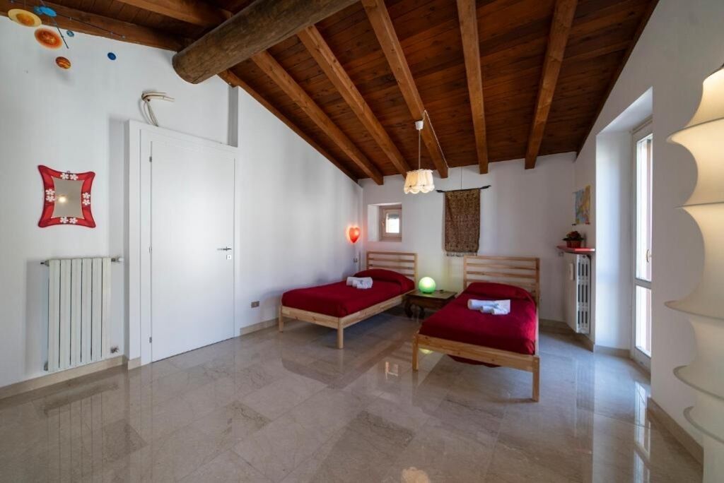 Une chambre avec deux lits en bois, une porte blanche, un radiateur et un plafond avec des poutres apparentes.