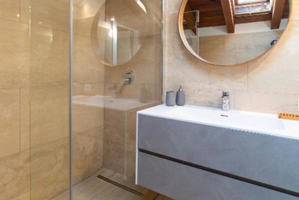 A modern bathroom with a glass shower enclosure, a round mirror, and a white vanity with a black stripe.