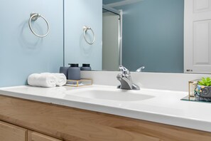 Une salle de bain moderne avec un lavabo blanc, un grand miroir et deux porte-serviettes fixés au mur.